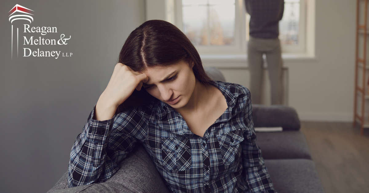 woman sad while man looks out window behind her